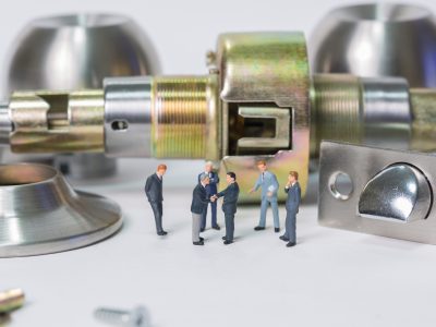 Selective focus of miniature businessman handshake with stainless steel round ball door knob components as commitment, business and locksmith concept.